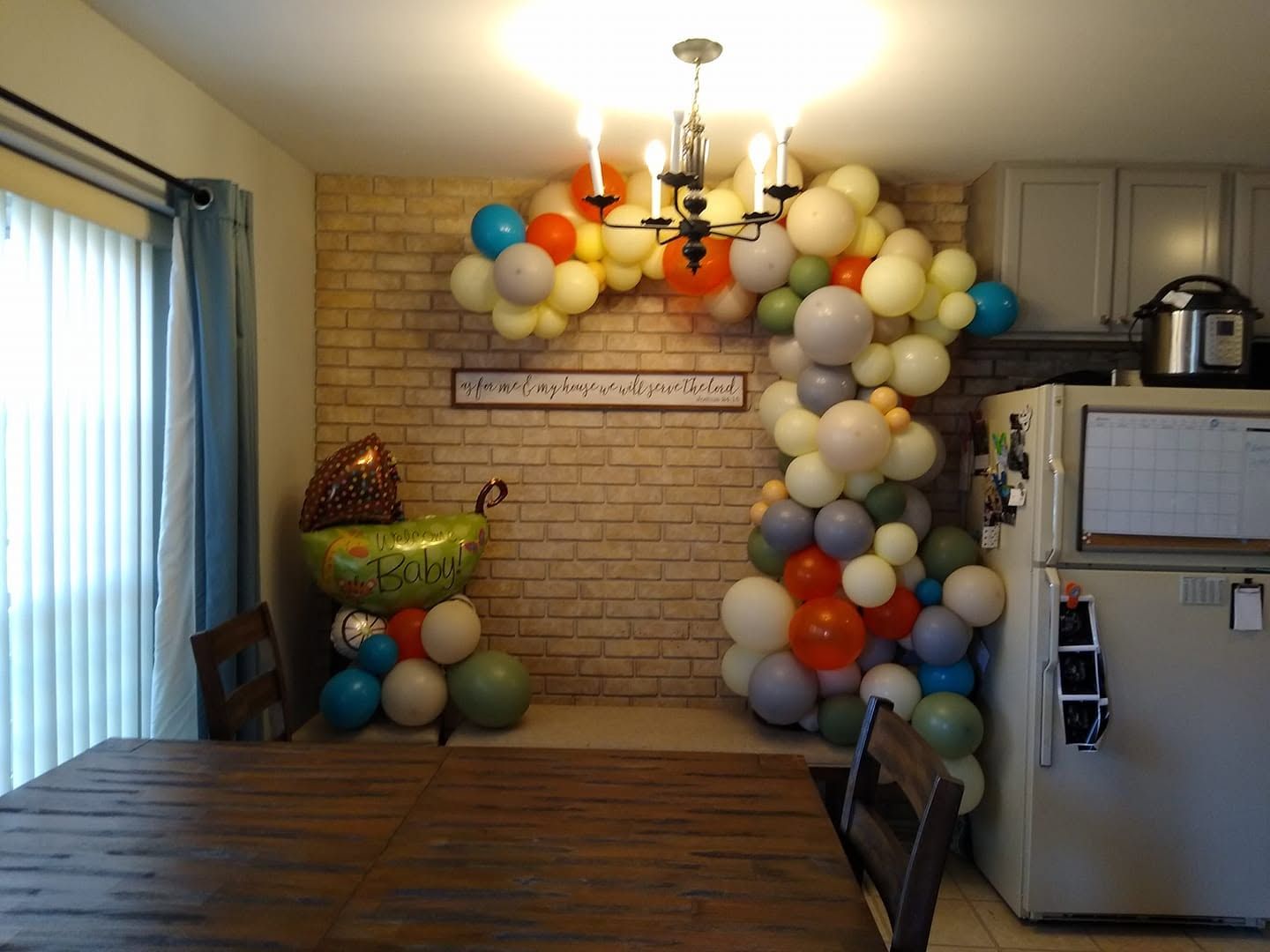 Balloon arch in a decorated room with table, brick wall, and kitchen counter.