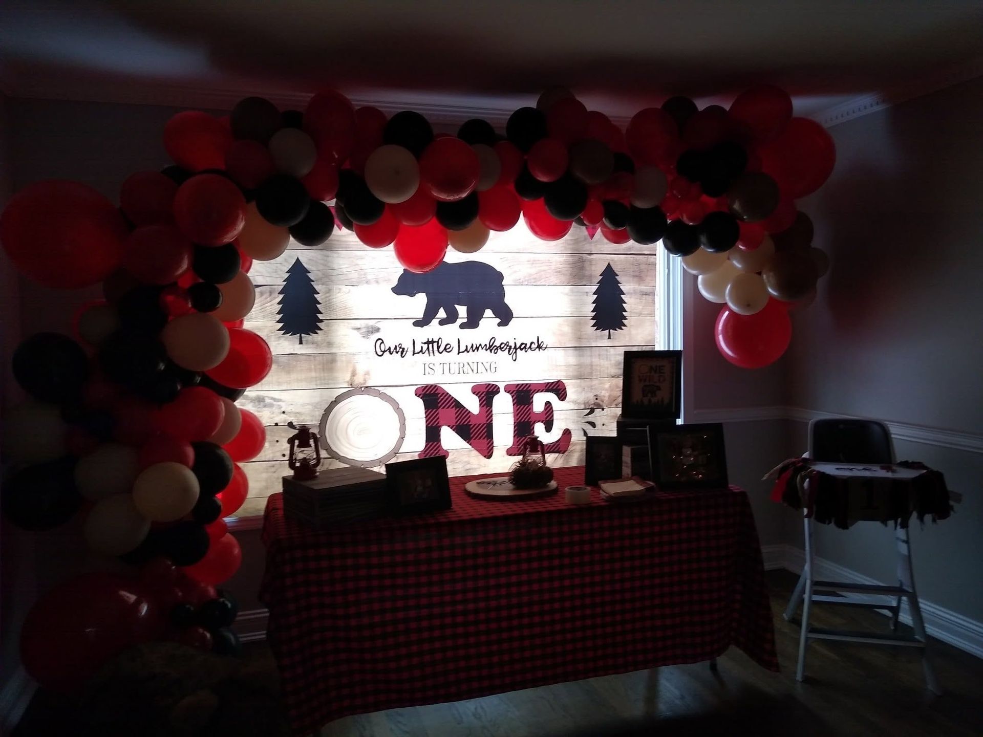 Red and black balloon arch over a Nebraska-themed table with a bear, trees, and a large “ONE” sign