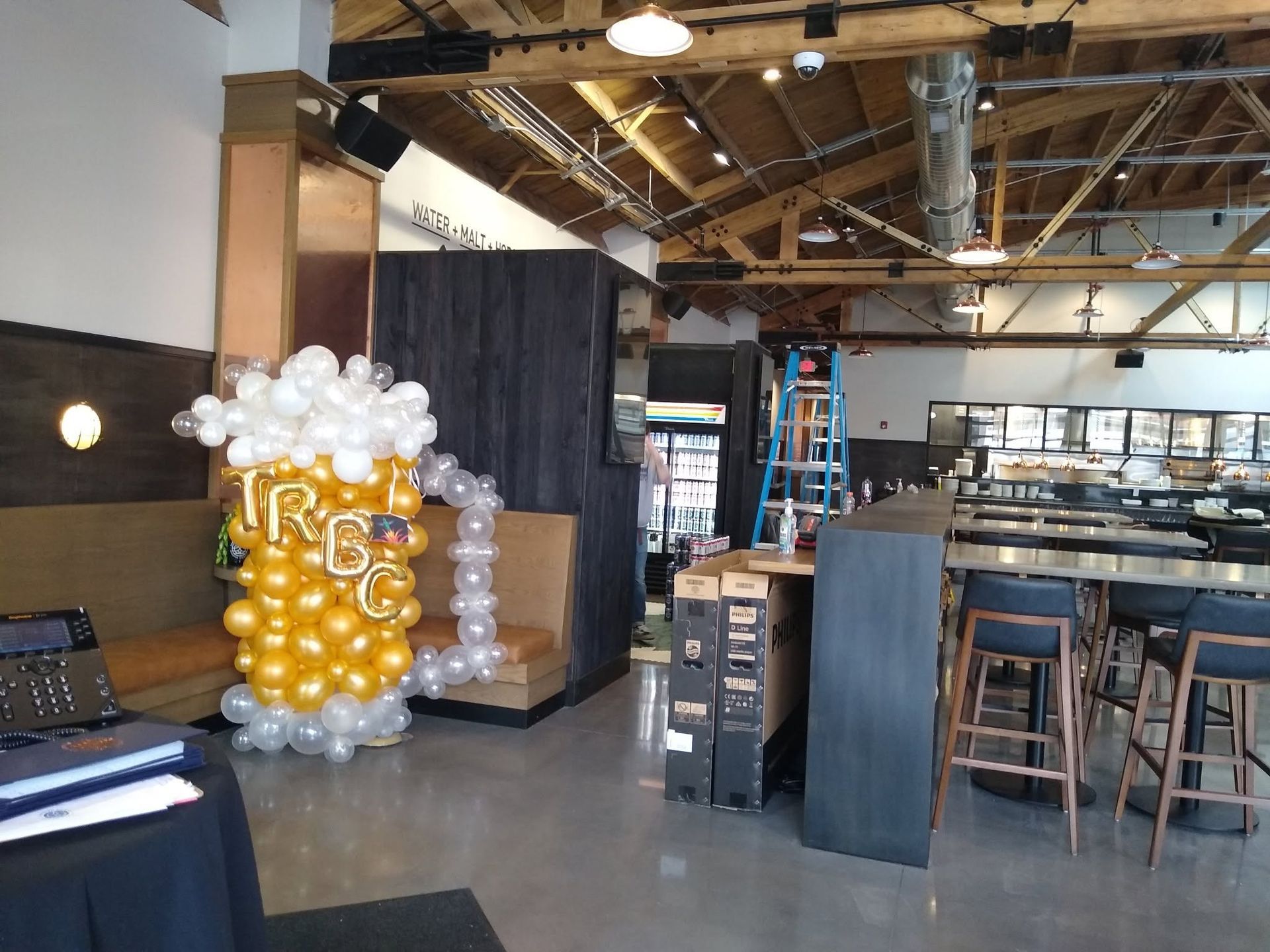 Industrial brewery taproom with gold-and-white balloon decoration and bar stools
