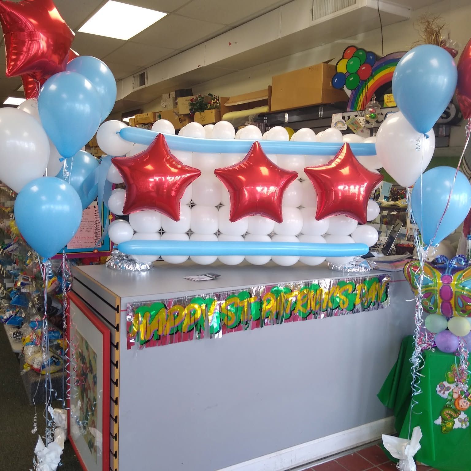 Birthday party setup with balloon garland, red stars, and a gray table in a store aisle