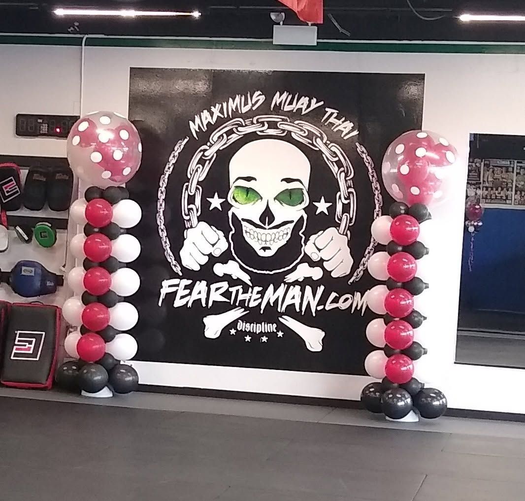 Gym entrance decorated with pink, black, and white balloon columns flanking a FearTheMan.com MMA banner.