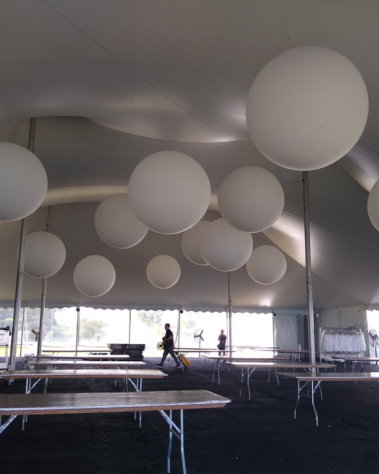 Large white balloons hanging inside a tented event space with people walking in the background