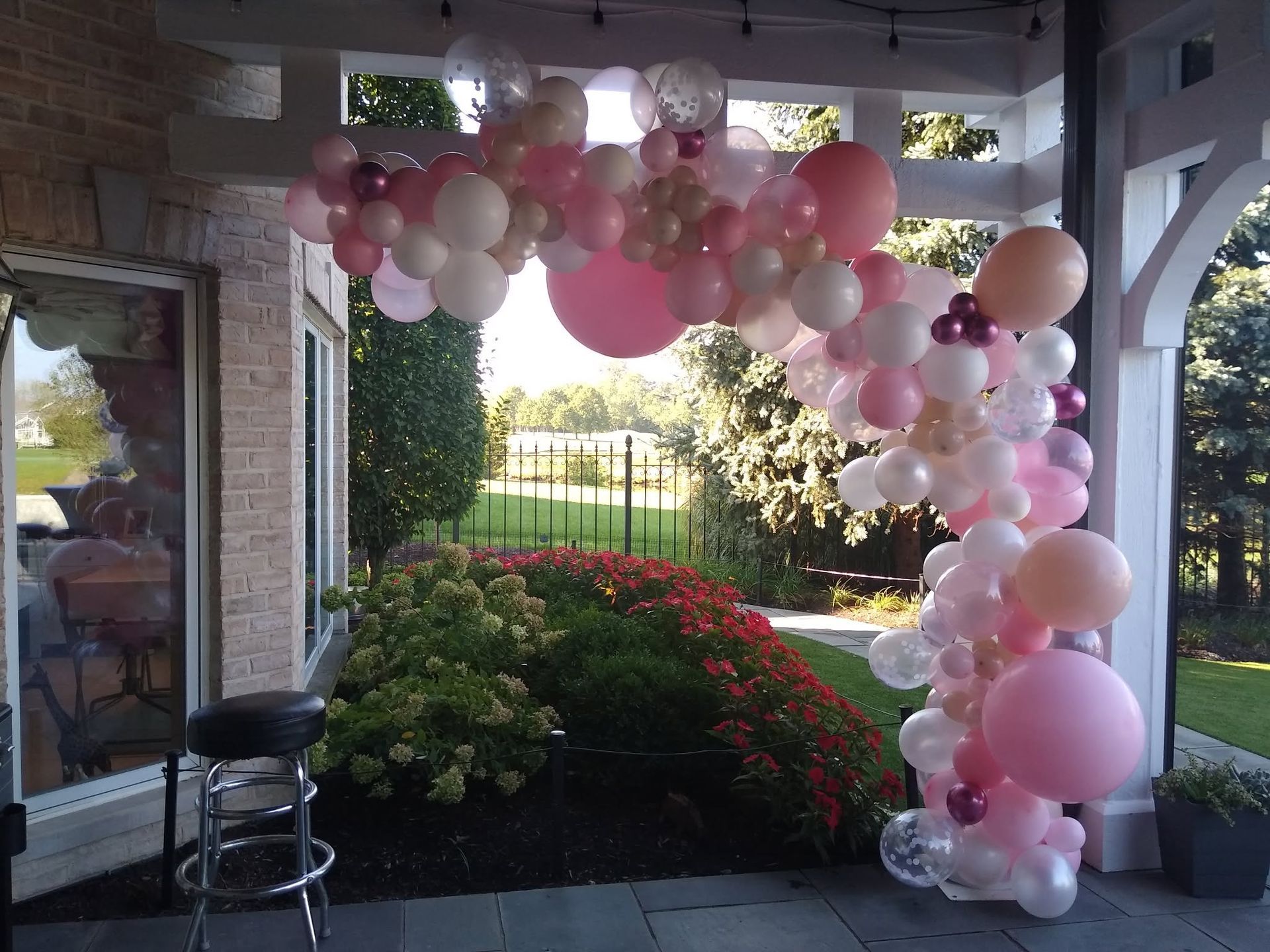 Pink and white balloon arch on a porch, framing a garden entrance