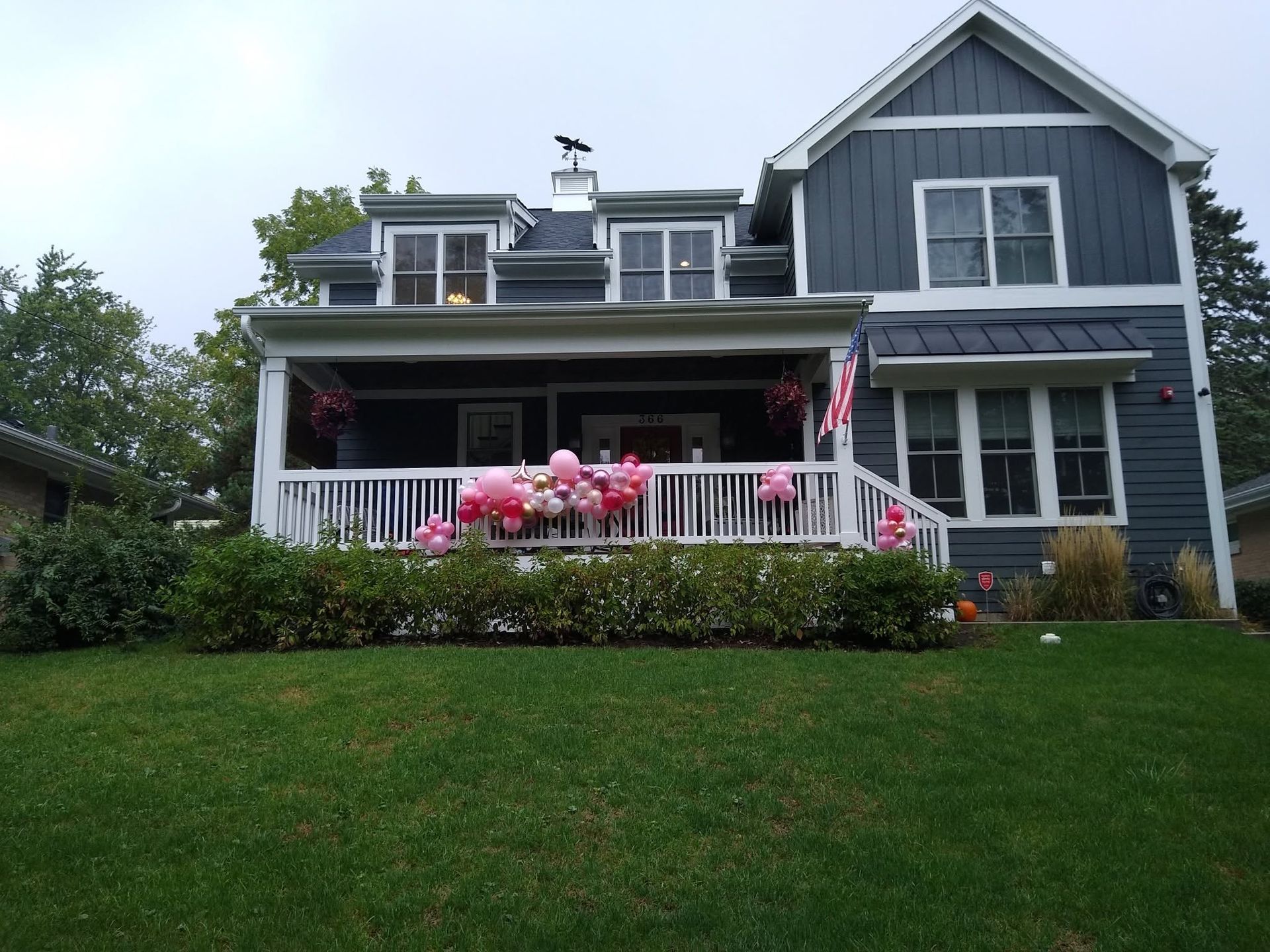 Two-story blue house with a front porch, pink flowers, and a green lawn