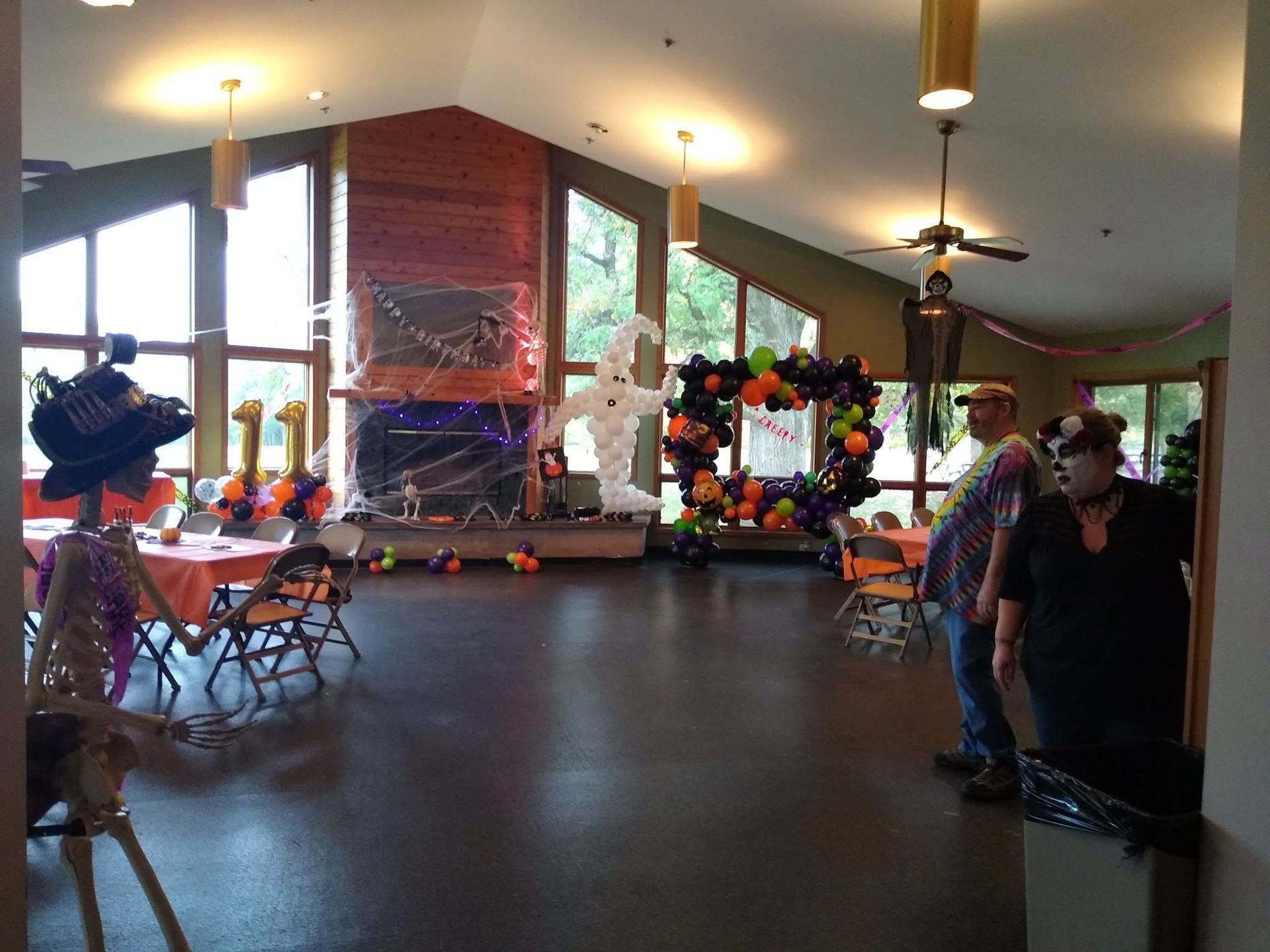 Decorated indoor hall with Halloween displays, tables, chairs, and people near large windows