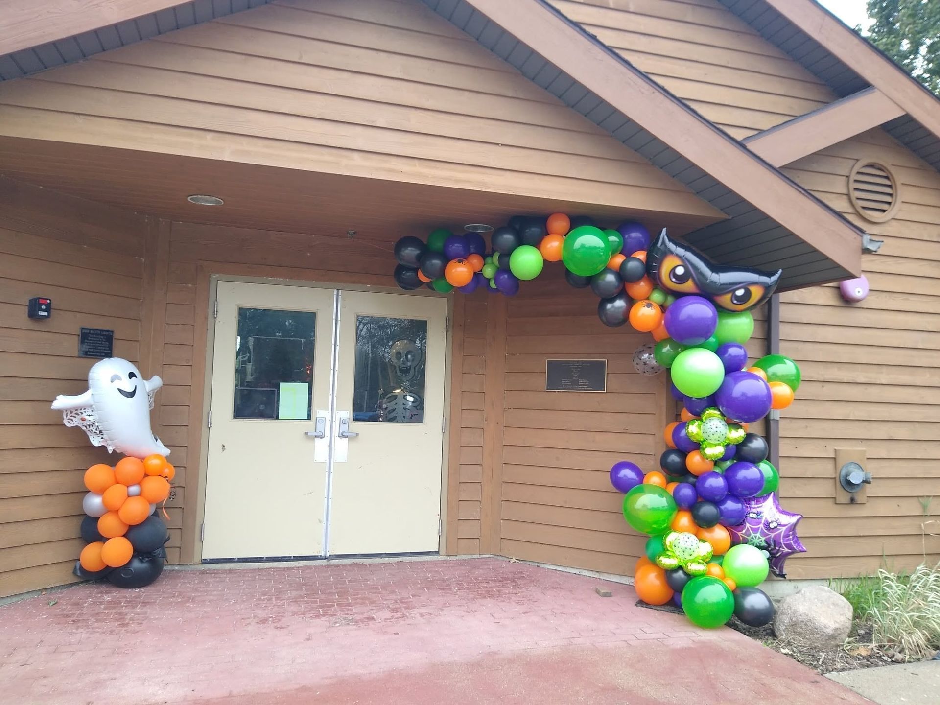 Halloween-decorated building entrance with ghost and balloon arch in orange, purple, green, and black
