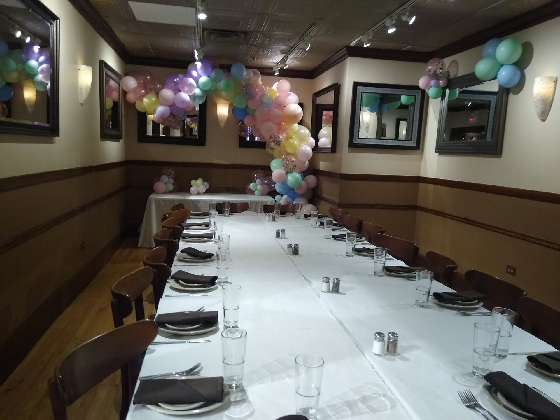 Decorated banquet table in a restaurant room with pastel balloon arch and place settings