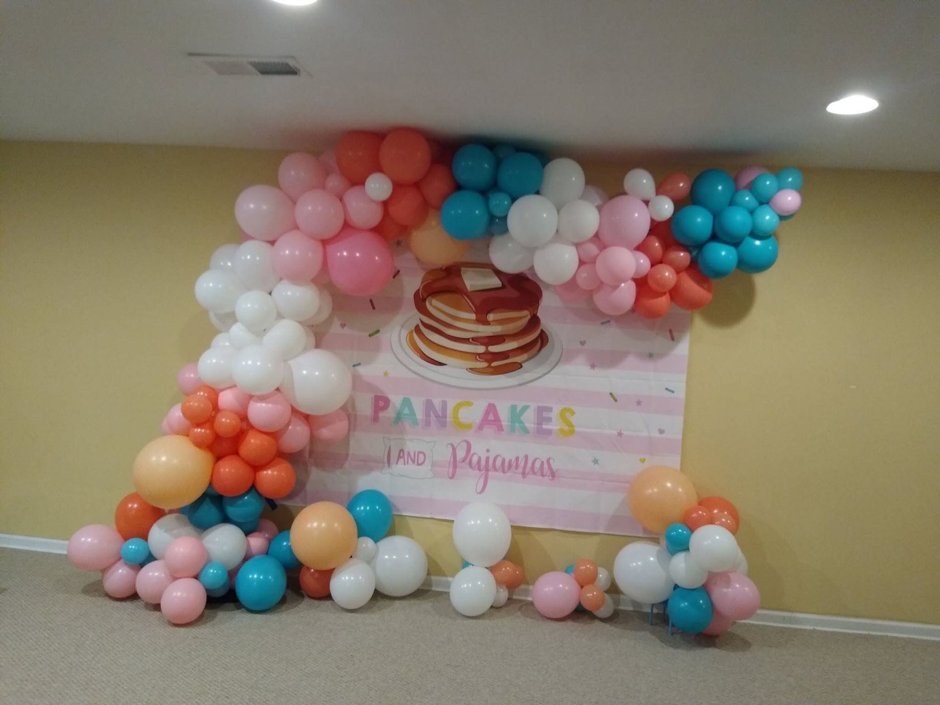 Pastel balloon arch framing a “Pancakes” party backdrop in a room