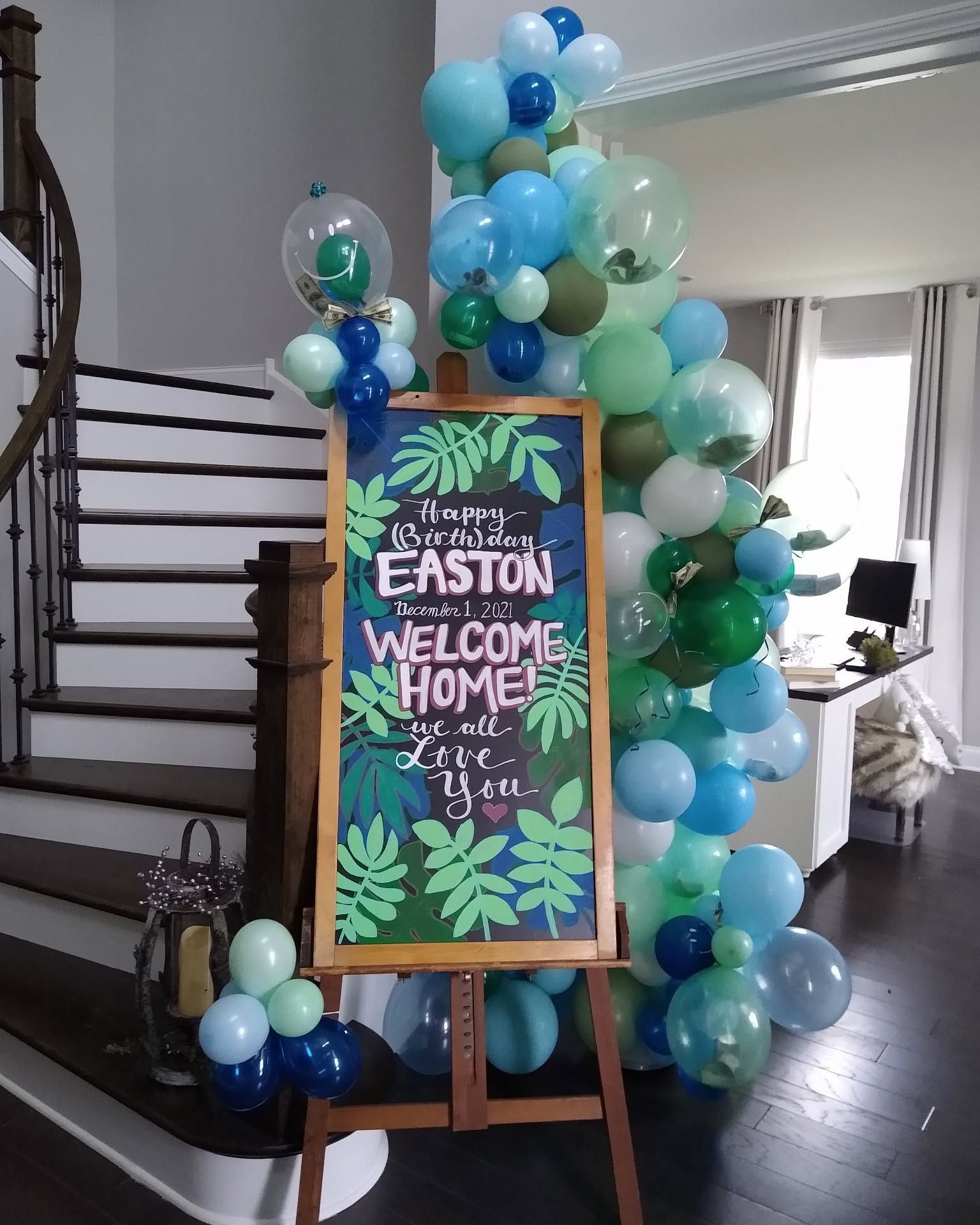 Balloon arch around a “Easton Welcome Home” sign on an easel in a doorway.