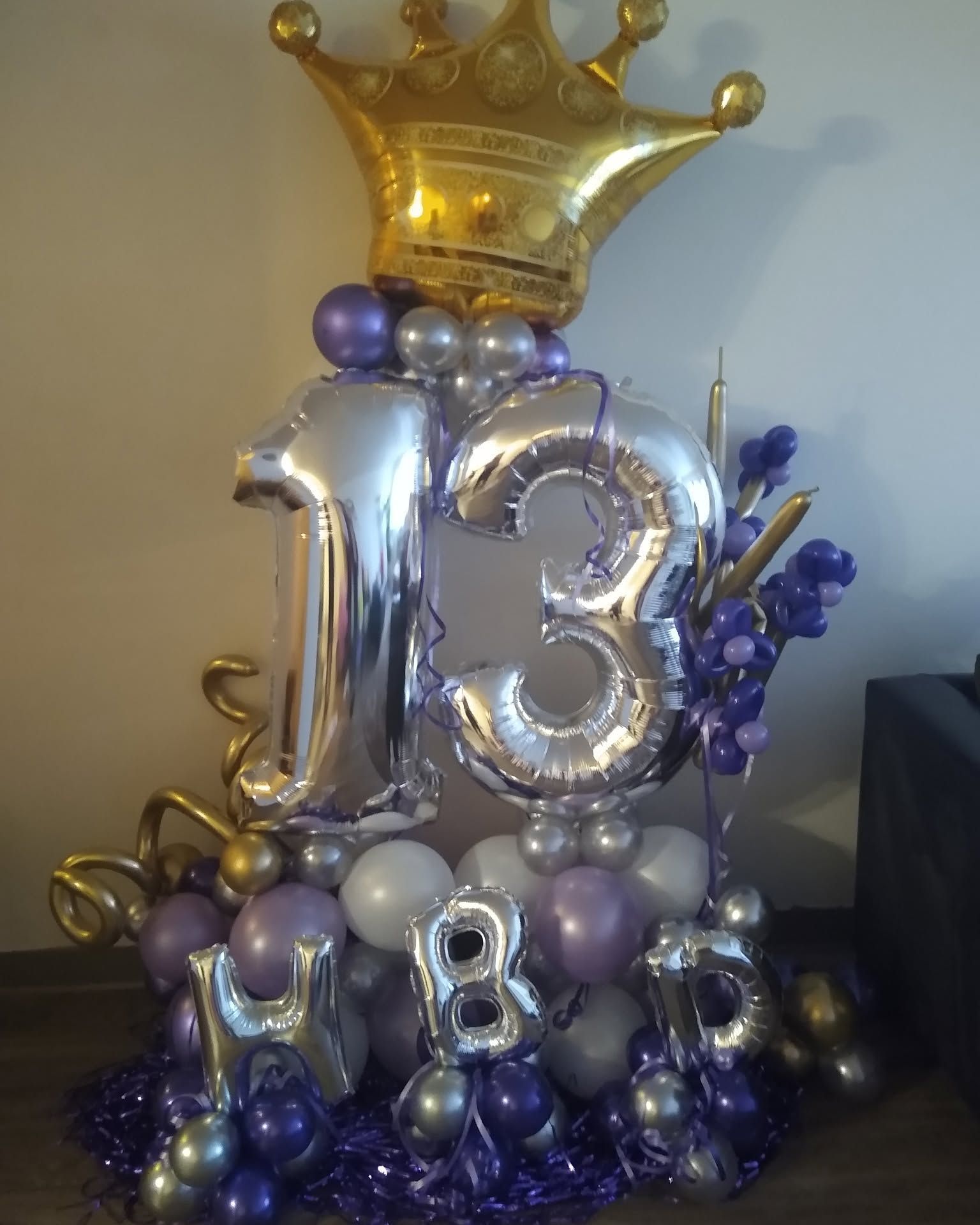 Silver and purple 13th birthday balloon display with gold crown and small “8” balloon base