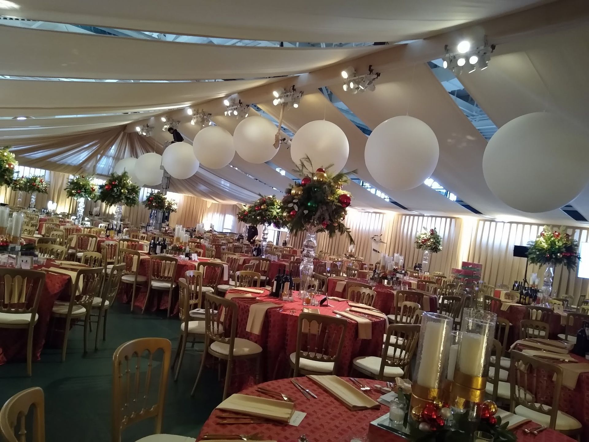 Decorated banquet hall with red tablecloths, white balloons, and overhead draped fabric.