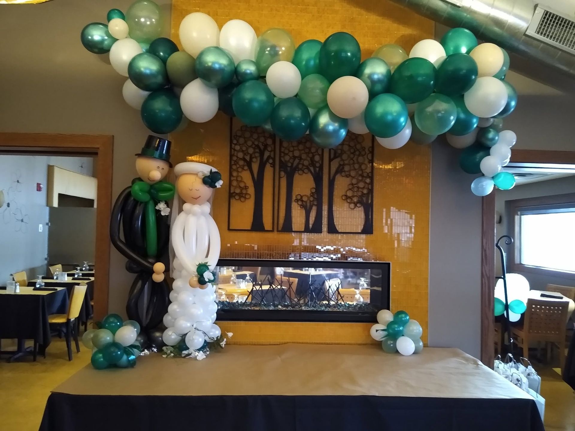 Balloon arch over a stage with two costumed figures and a lit fireplace backdrop