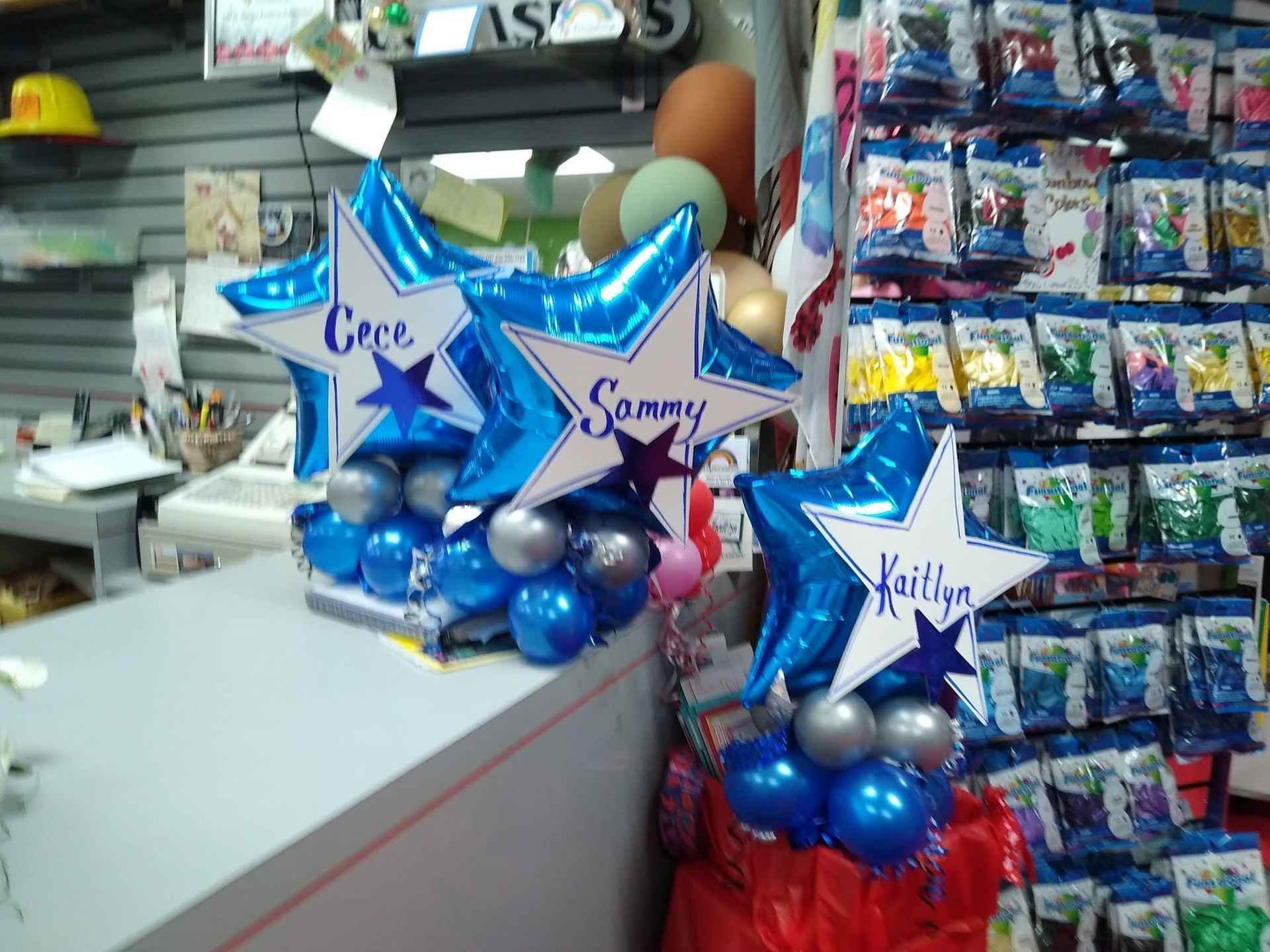 Star-shaped blue and silver balloon bouquets with names, displayed at a store counter next to candy shelves.