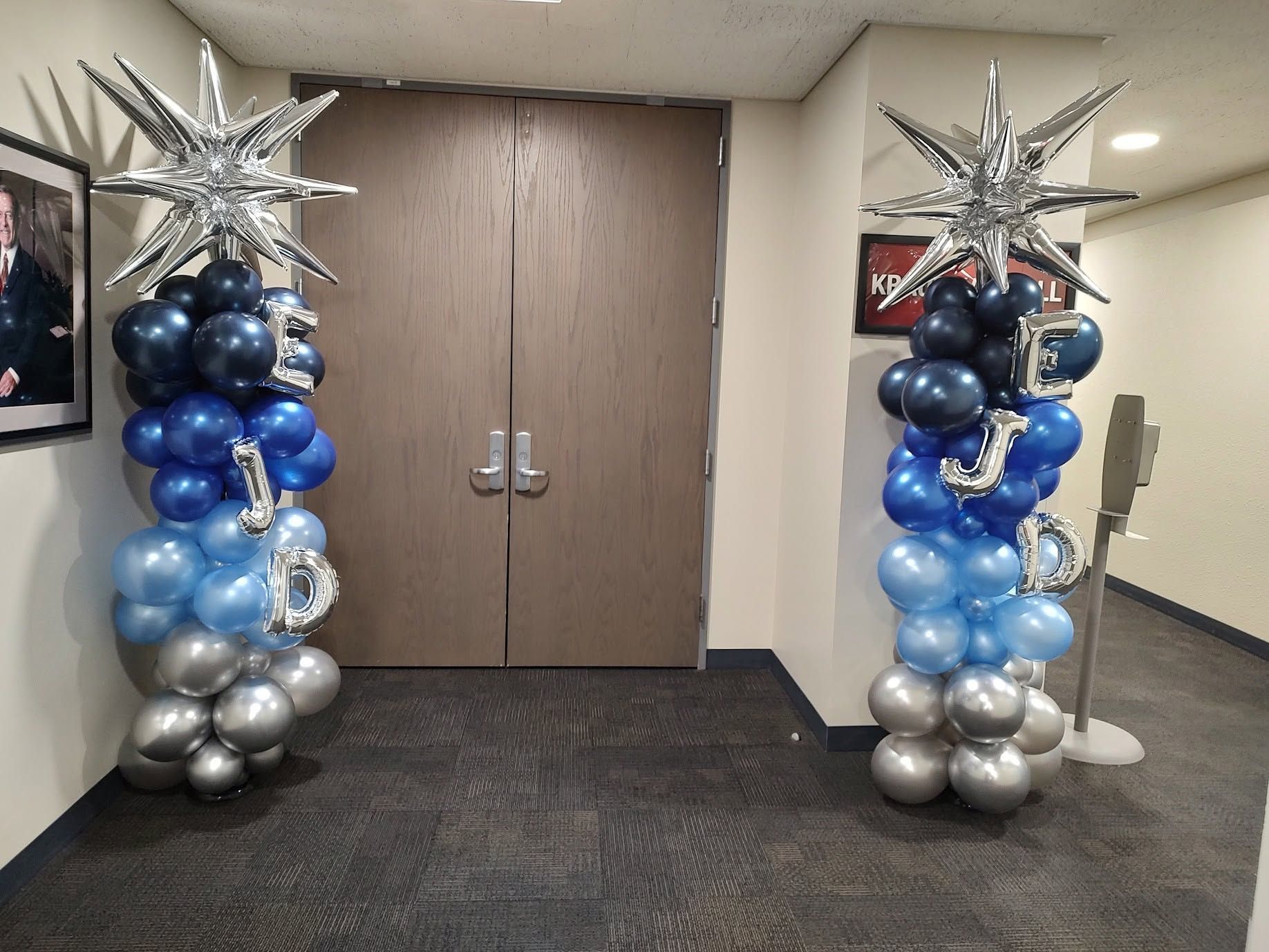 Hallway entrance decorated with blue, silver, and black balloon columns topped with starburst balloons