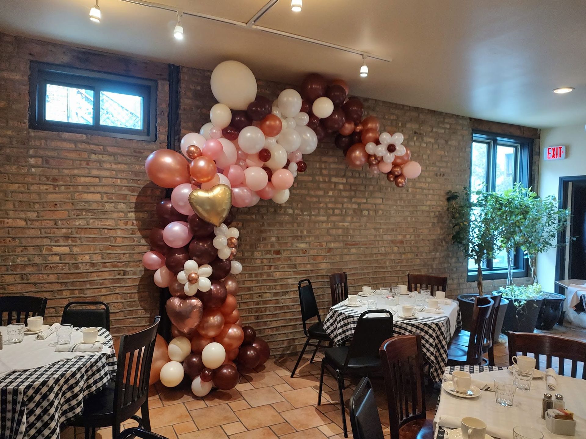 Balloon garland in pink, white, and copper against a brick wall in a decorated dining room