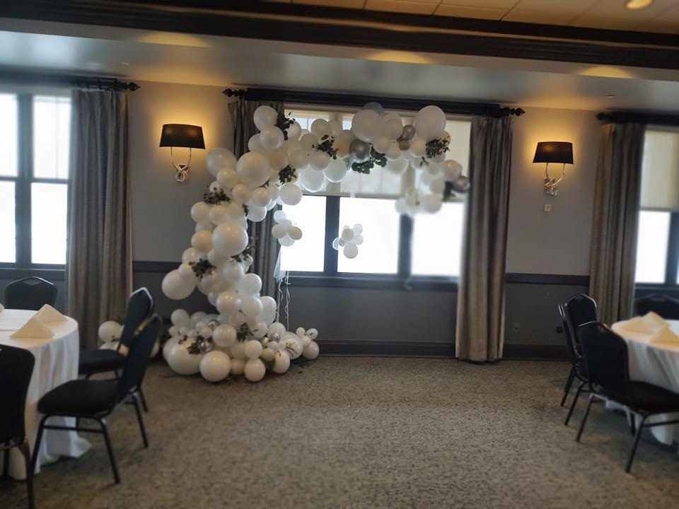 Balloon arch decorates a room with tables by the windows and carpeted floor.