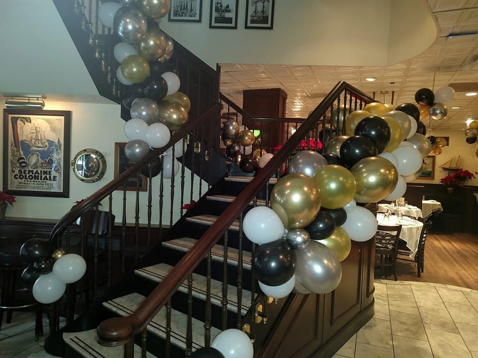 Staircase in a decorated banquet hall with black, white, and gold balloon garlands at the railings