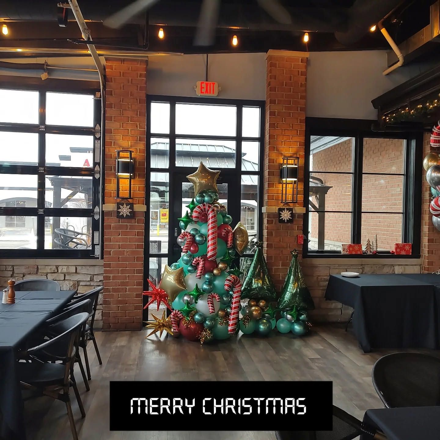 Decorated Christmas tree display in a brick-walled restaurant with a “Merry Christmas” sign