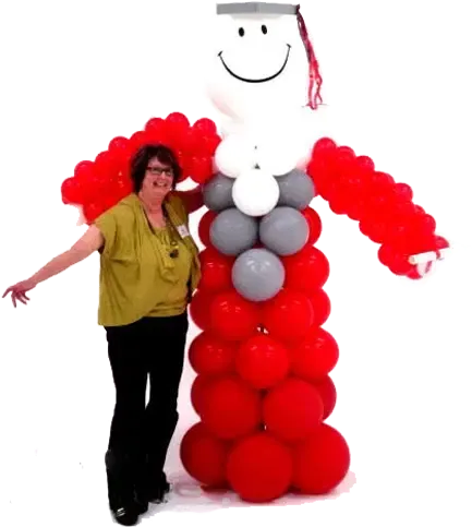 Woman standing beside a red, white, and gray balloon sculpture shaped like a smiling figure with a graduation cap