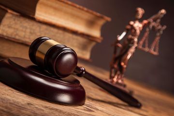 Martello del giudice su un blocco di legno con la statua della dea della giustizia sullo sfondo di una biblioteca giuridica.