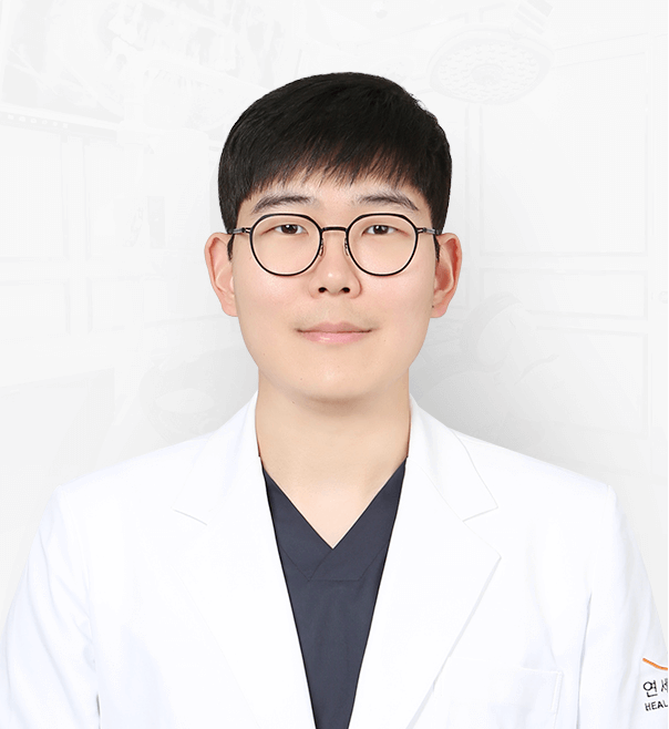 Young man in glasses and a white coat, possibly a doctor, facing the camera.