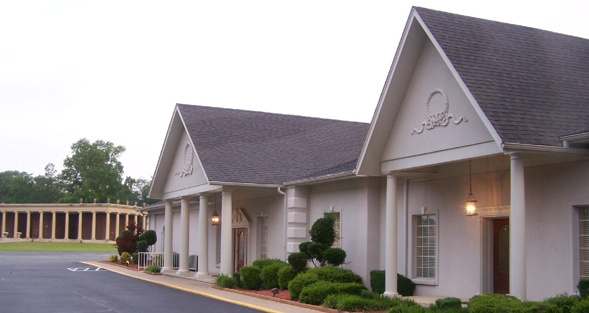 Single-story beige office building with gabled roofs, manicured shrubs, and a parking lot at dusk