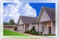 Modern church building with white columns and a blue sky, surrounded by green lawn