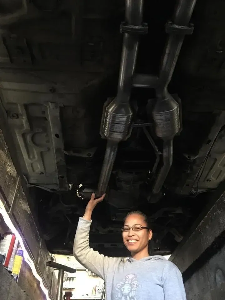 A woman is standing underneath a car in a garage | Ed Hanson's Muffler Service