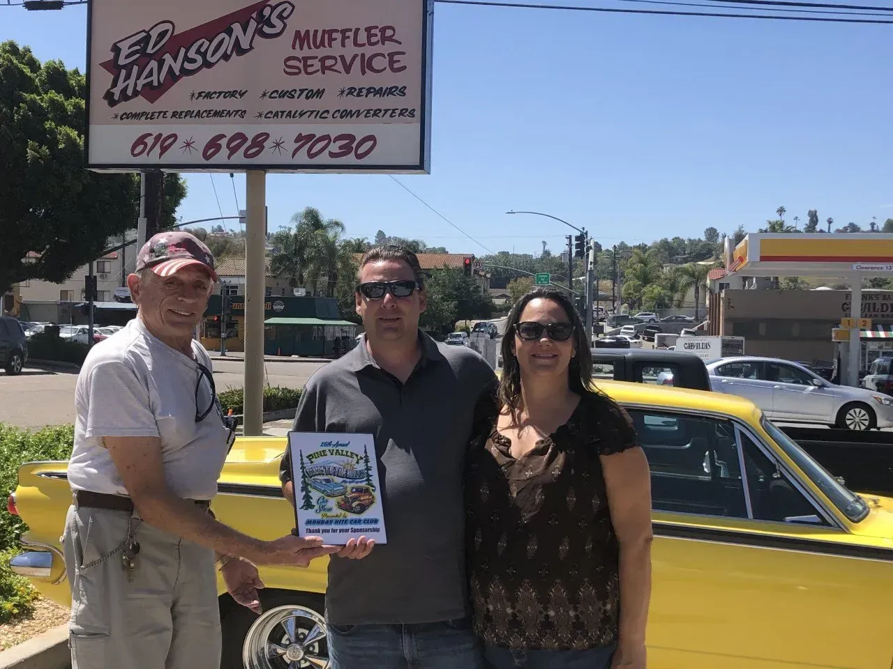 Three people shaking hands in front of a yellow car | Ed Hanson's Muffler Service