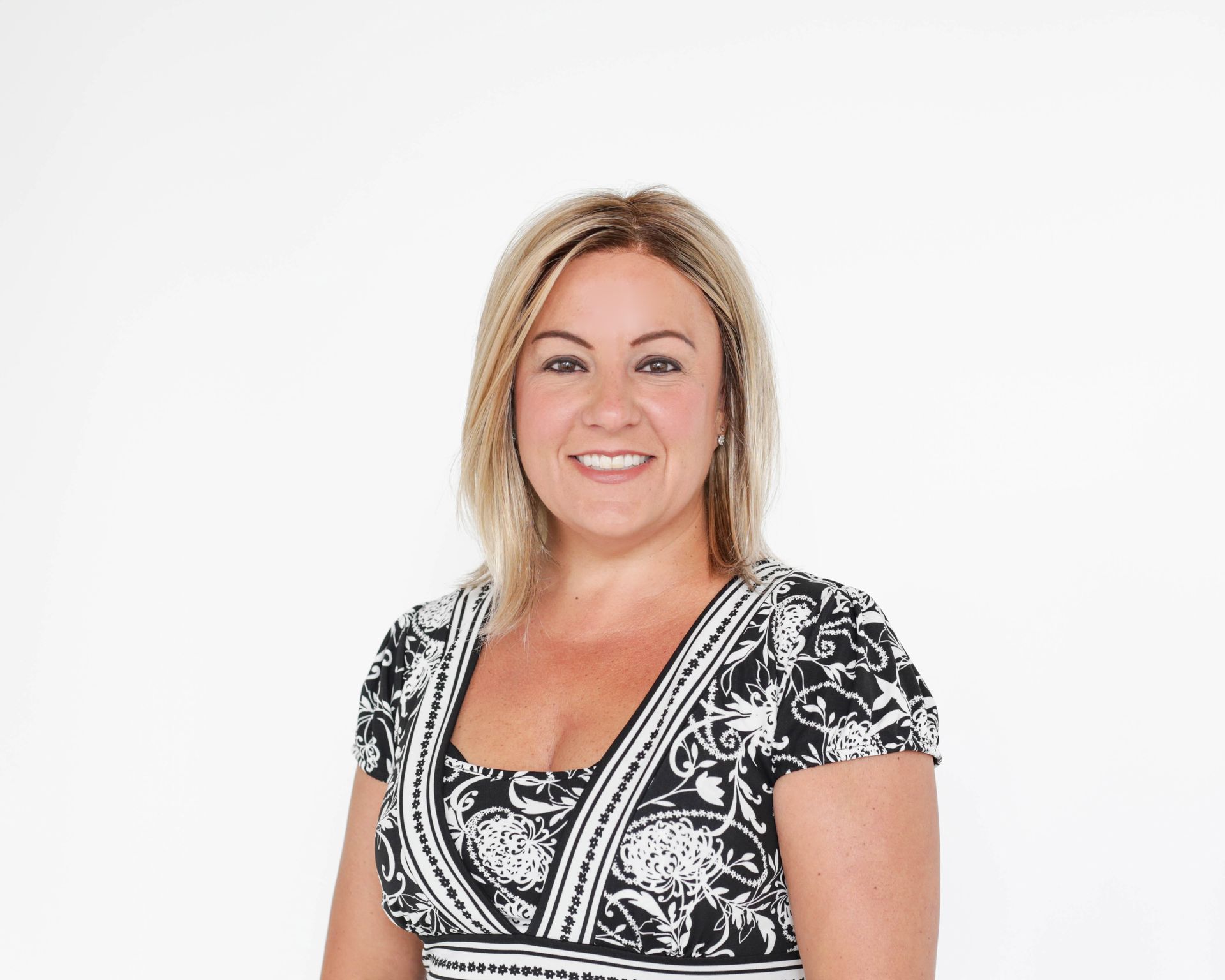 A smiling person with shoulder-length blonde hair wearing a black and white patterned dress against a white background.