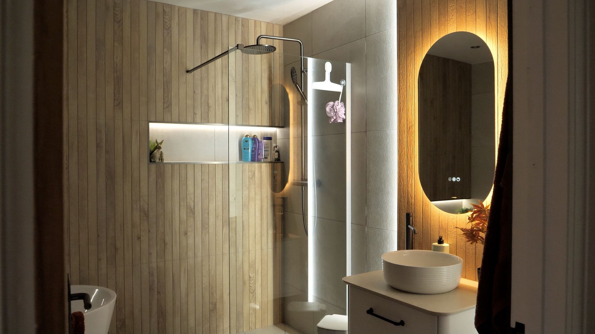 Modern bathroom with wood paneling, shower, and illuminated mirror.