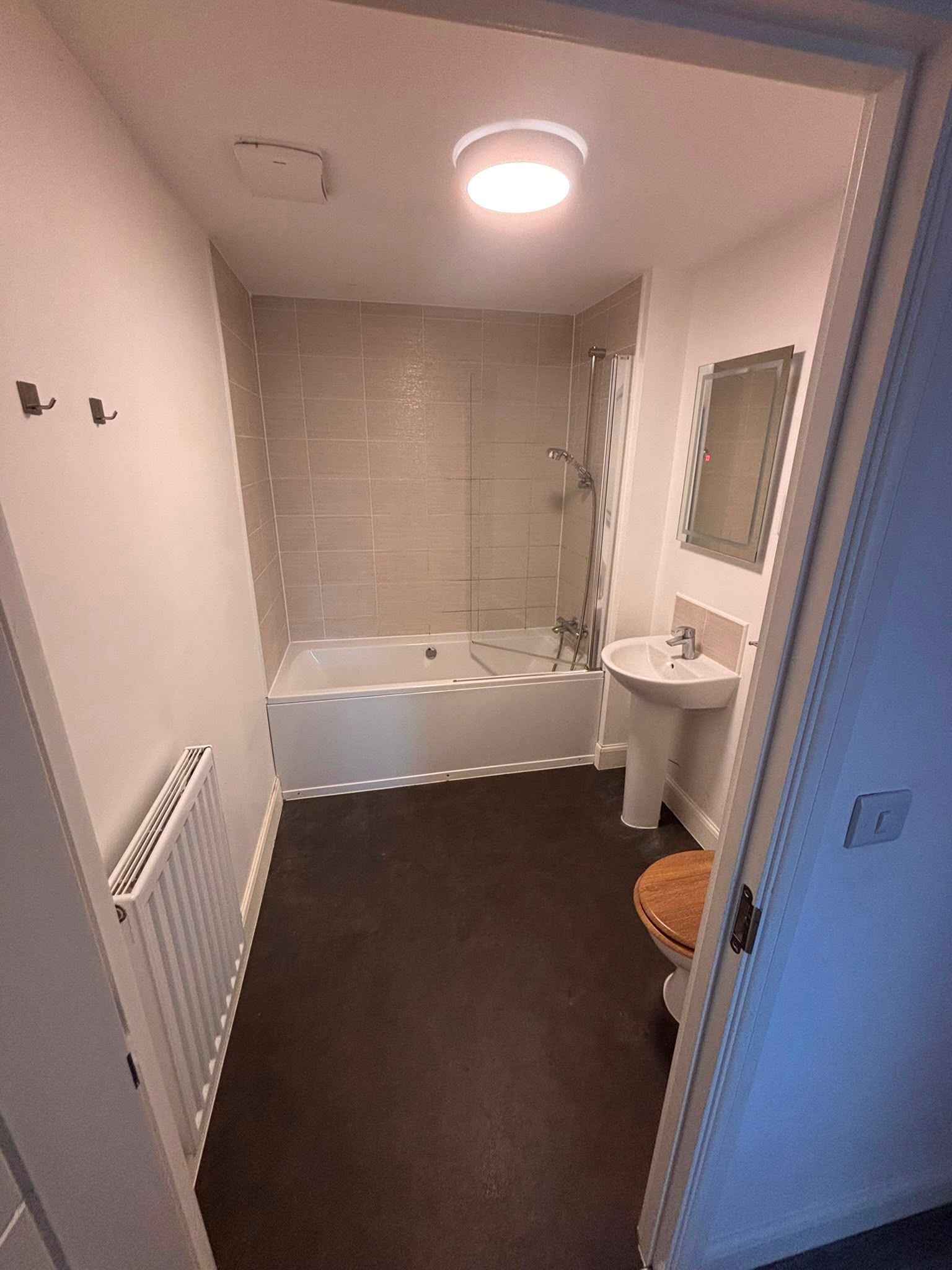 Bathroom before renovation with pedestal basin, shower over bath and dark flooring