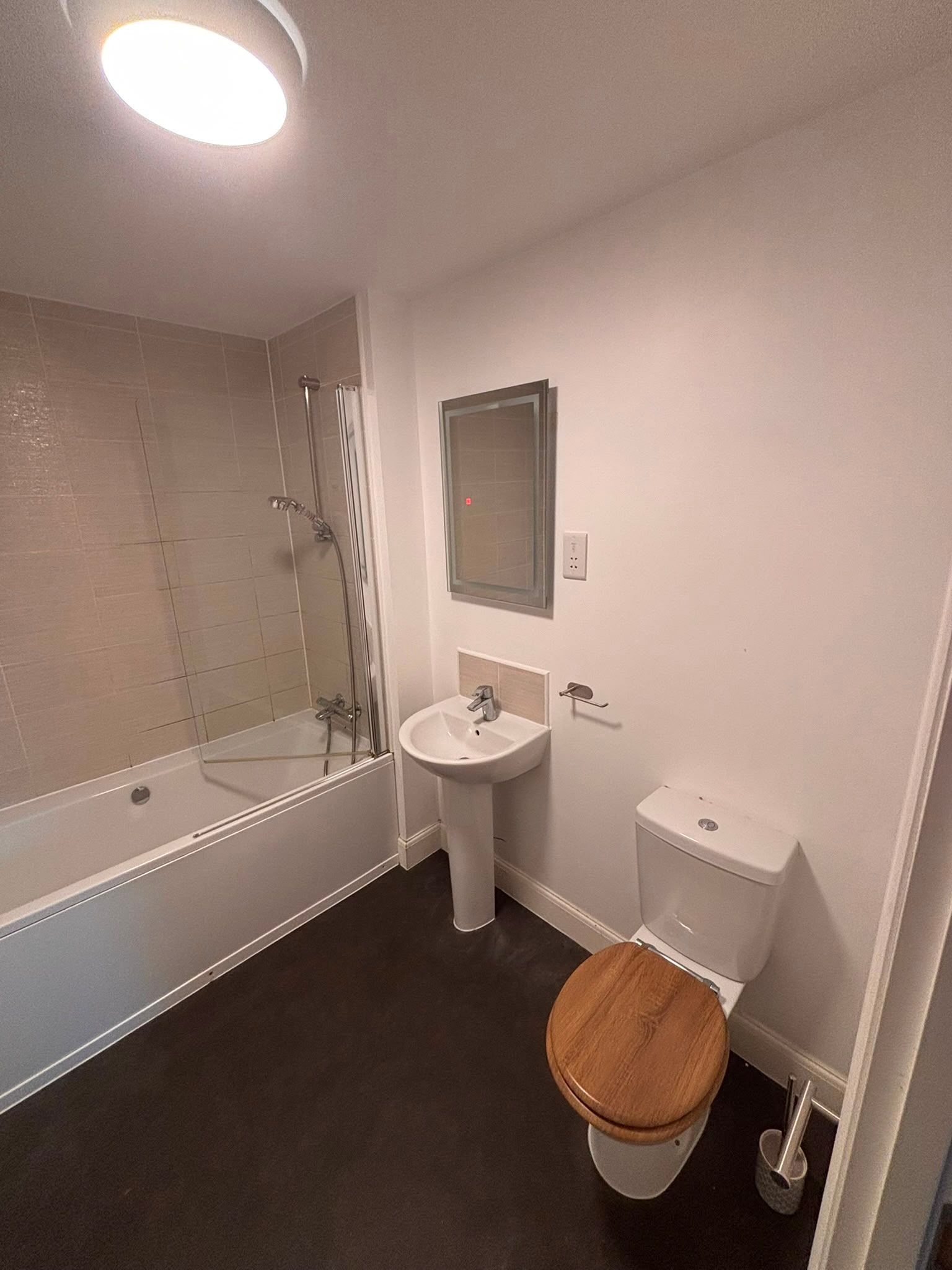 Bathroom before renovation with pedestal basin, shower over bath and dark flooring