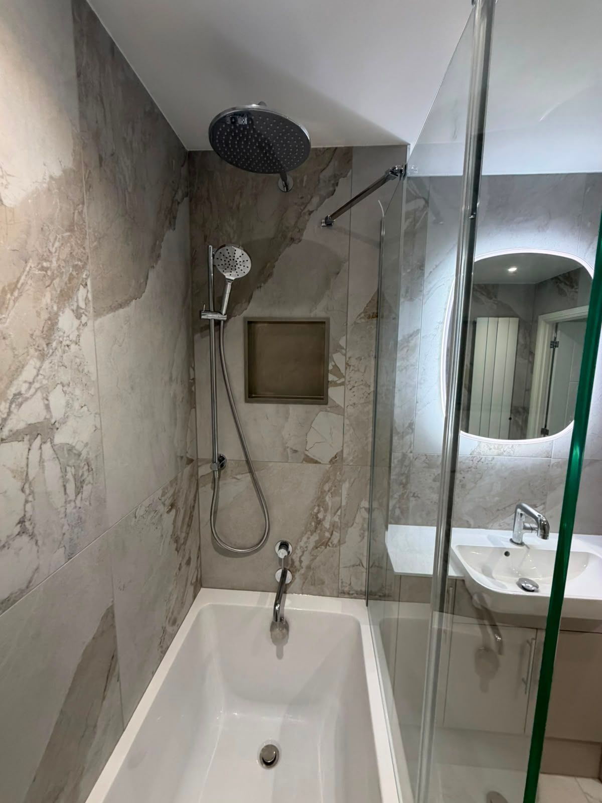 Modern shower over bath with recessed storage niche, rainfall shower head and large format stone effect bathroom tiles