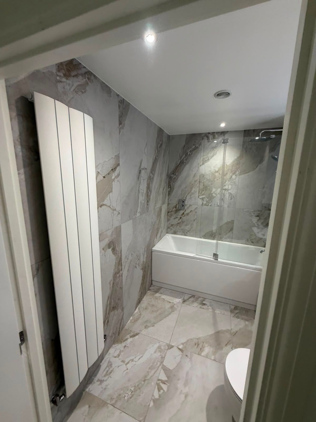 Bathroom renovation with large format stone effect tiles, shower over bath and tall heated towel radiator by My Life Interiors