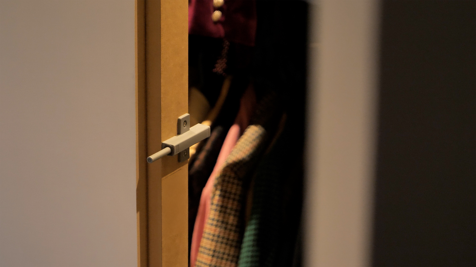 Open closet with clothes, white bolt latch, wood door frame.