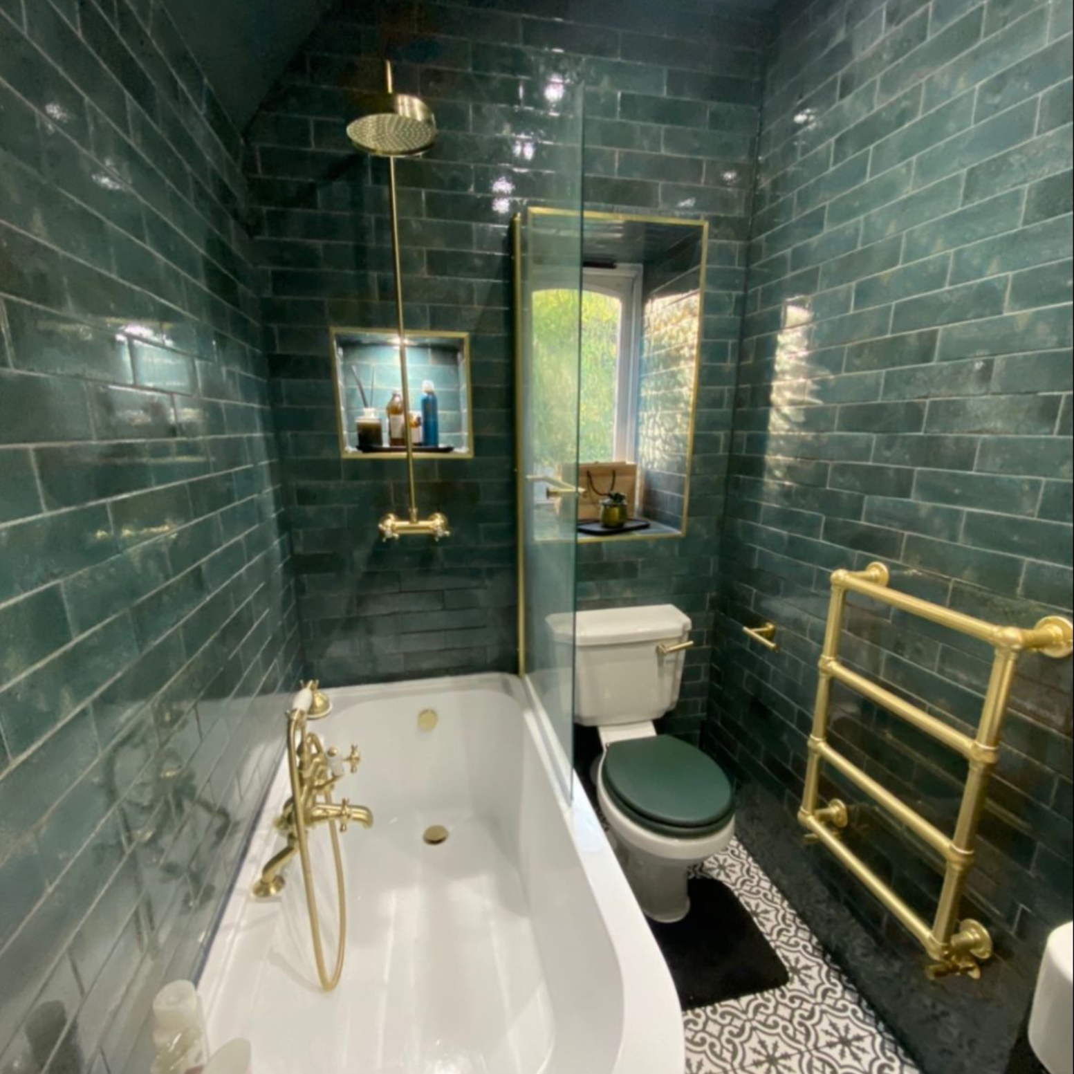 Green-tiled bathroom with gold fixtures: bathtub, shower, toilet, and towel rack.