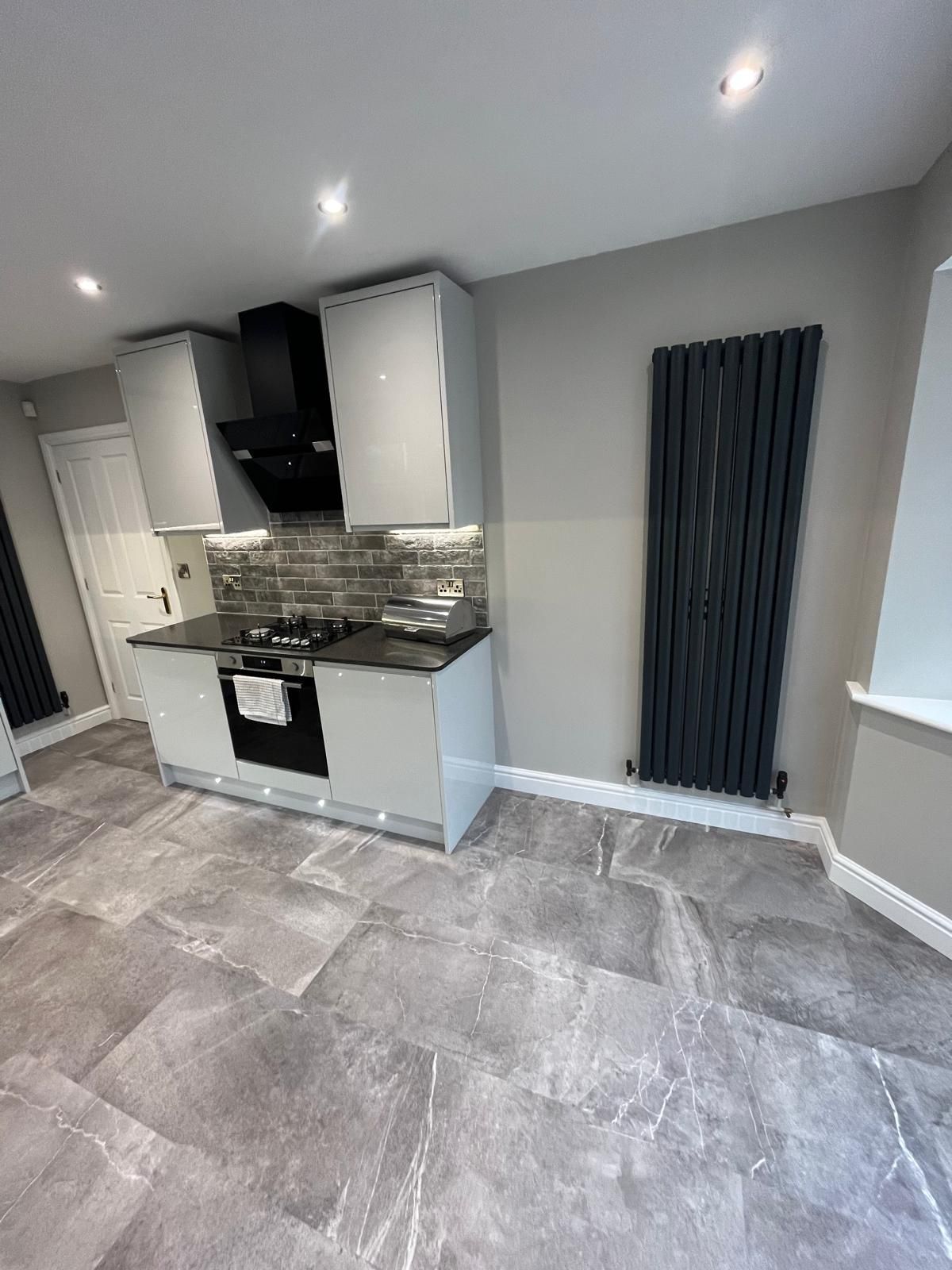 Bespoke kitchen design with dark grey fitted cabinets, central island with seating, integrated double ovens and white worktops