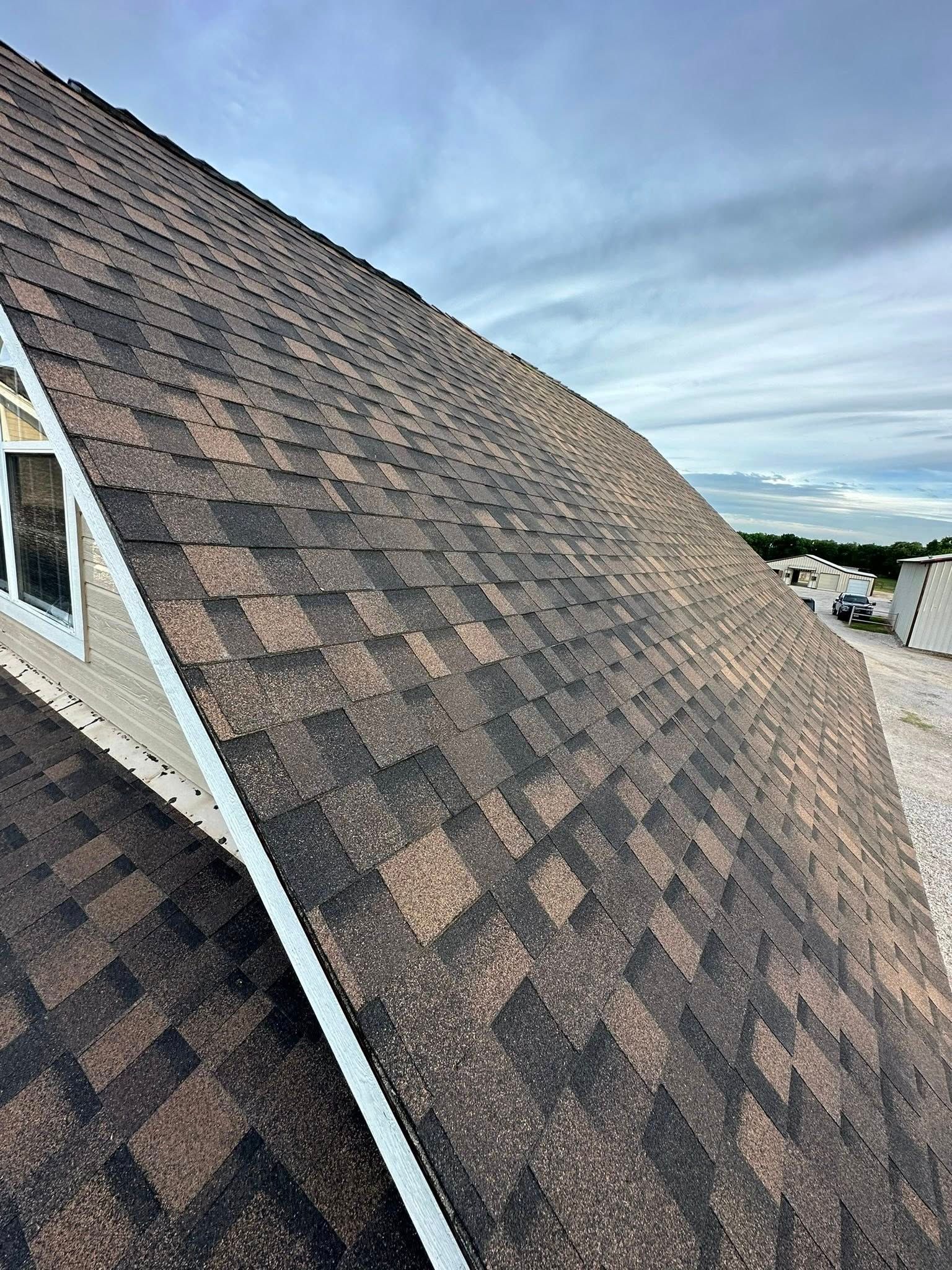 Close-up of a shingled roof with a dormer window under a cloudy sky