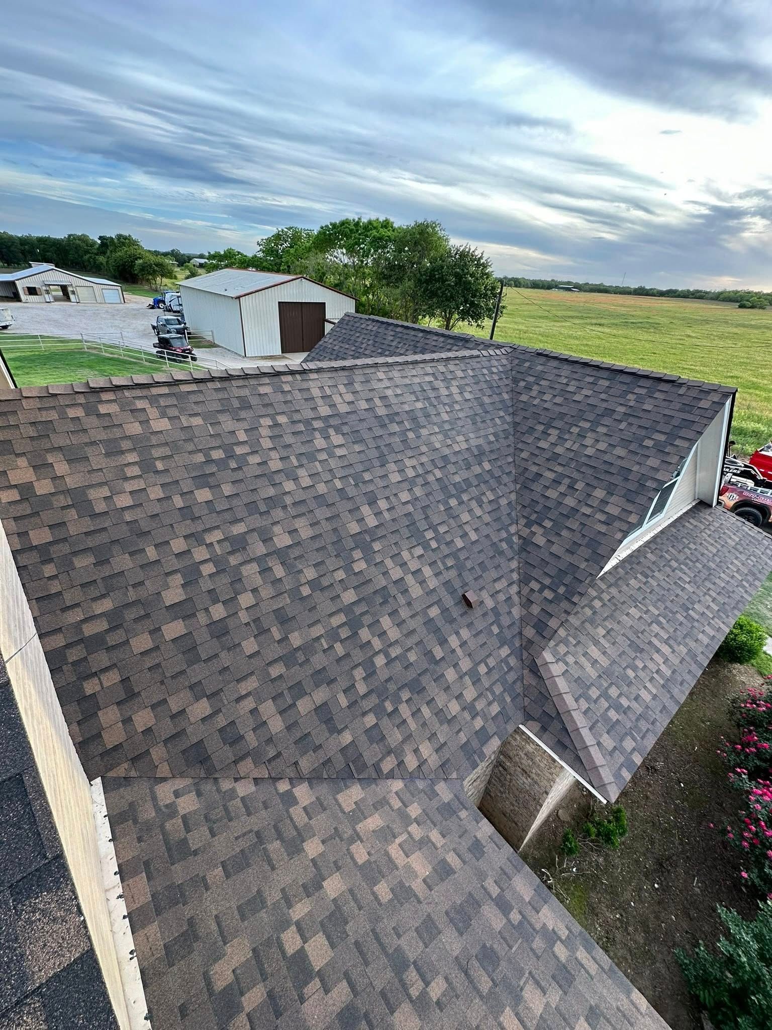 Aerial view of a shingled house roof with multiple slopes and a rural landscape beyond.