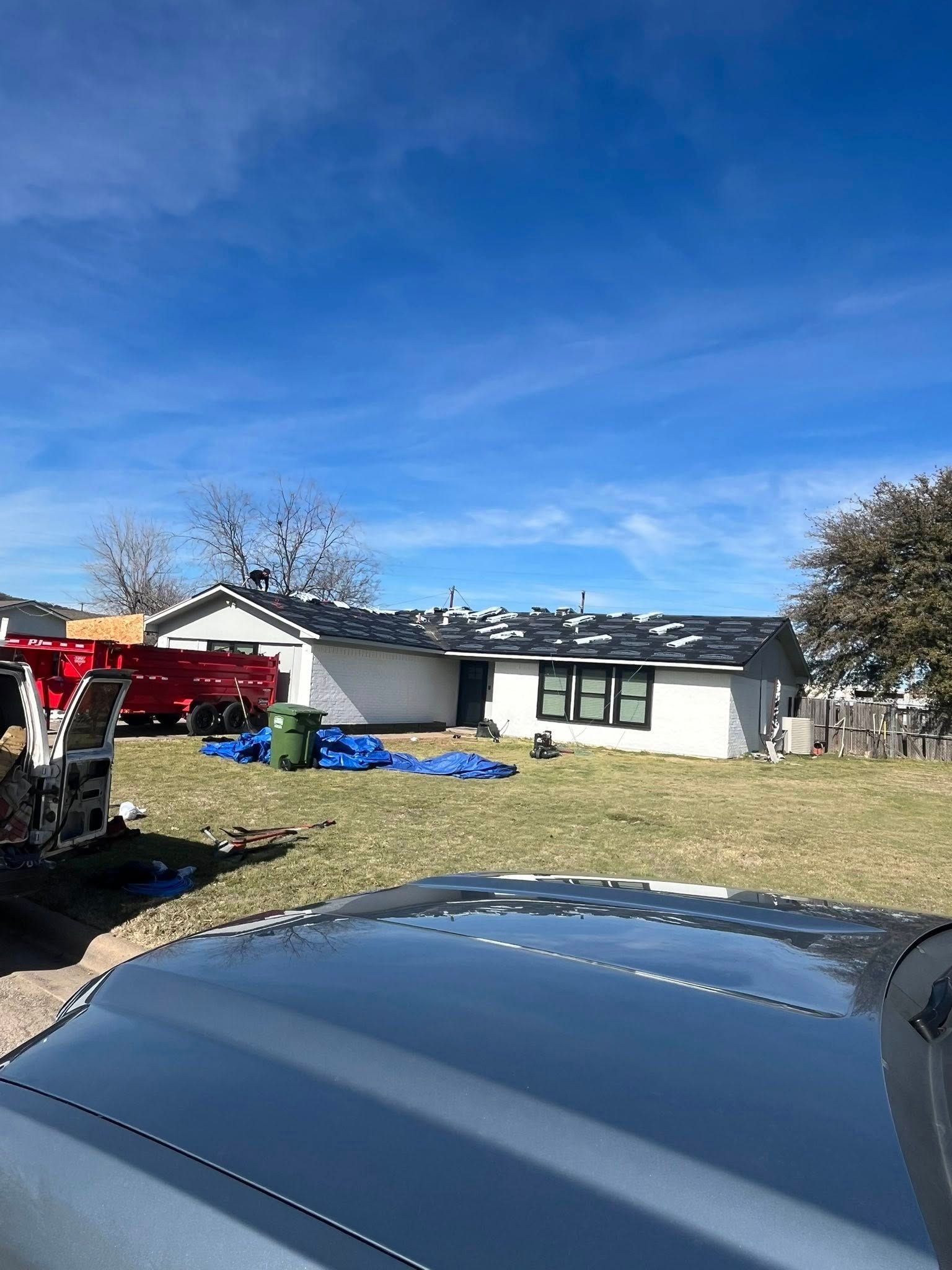 Suburban house with lawn, blue tarp, and parked vehicles under a clear blue sky