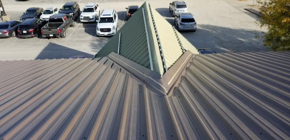 Rooftop metal panels leading to a green triangular skylight above a parking lot