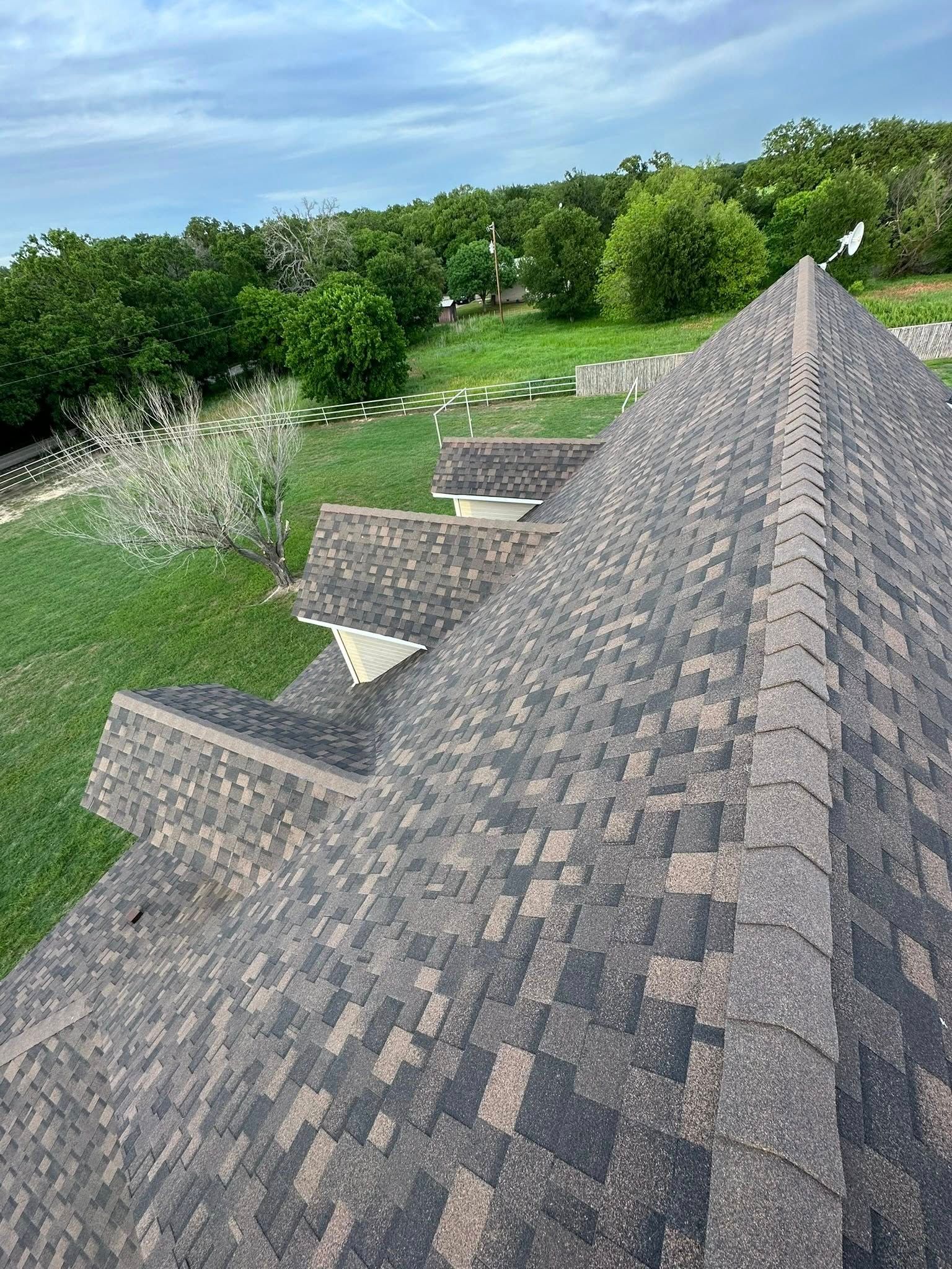 Steep shingled roof overlooking a green hillside and trees under a bright sky