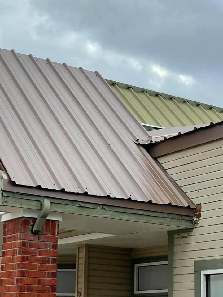 Residential house roof with brown and green metal panels above a brick wall and siding