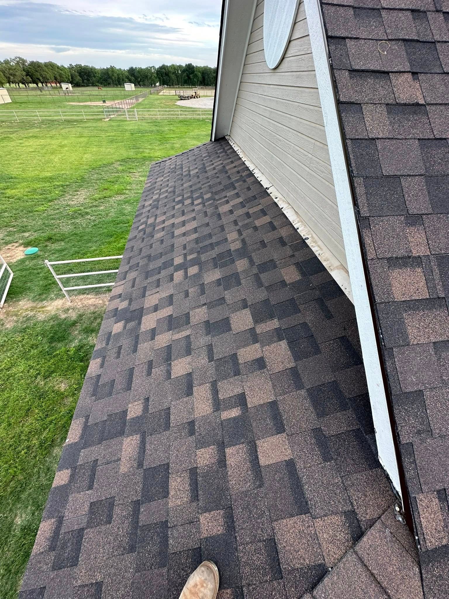 Roof shingles beside a white house wall, with a grassy field in the background.