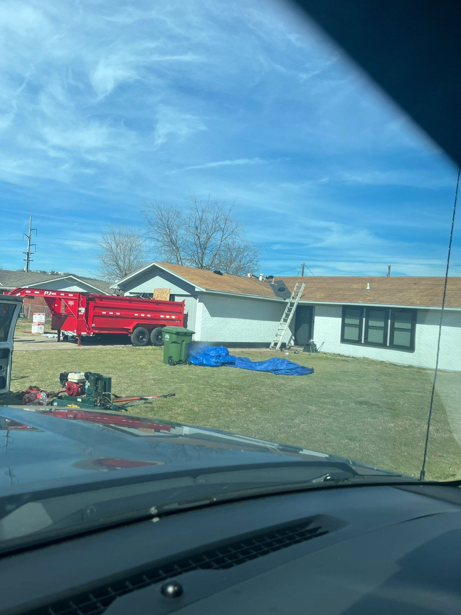 Red fire truck beside a single-story house with blue tarp in front yard, viewed from a car