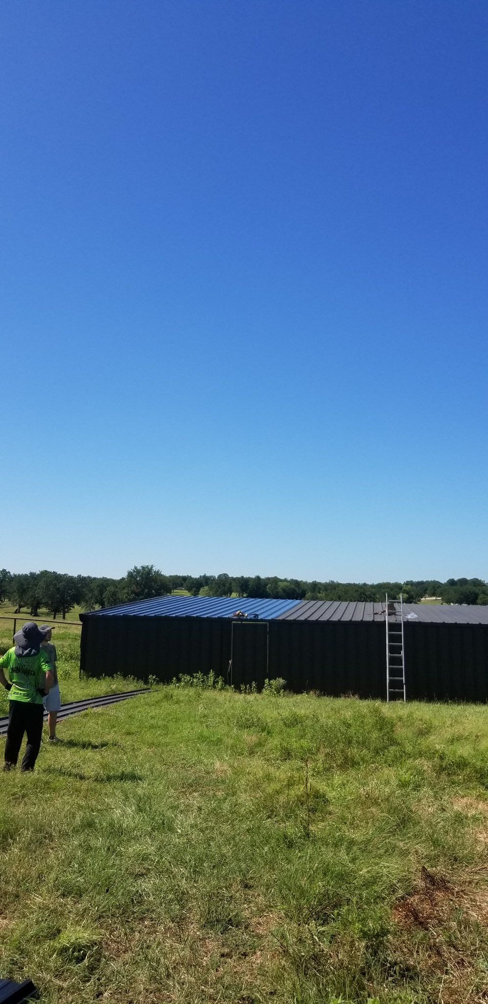 Solar panels on a grassy field under a clear blue sky, with a person in a hi-vis vest at left.