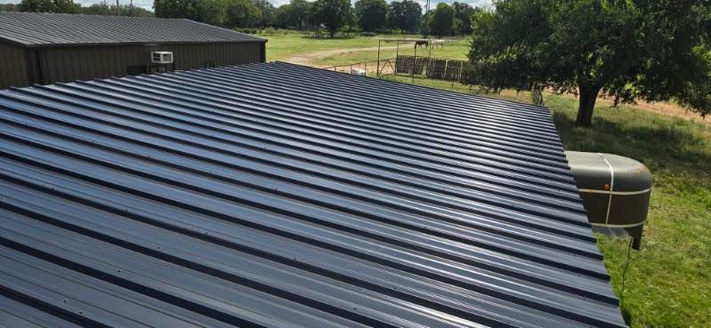 Black corrugated metal roof on a building with grassy yard and trees in the background