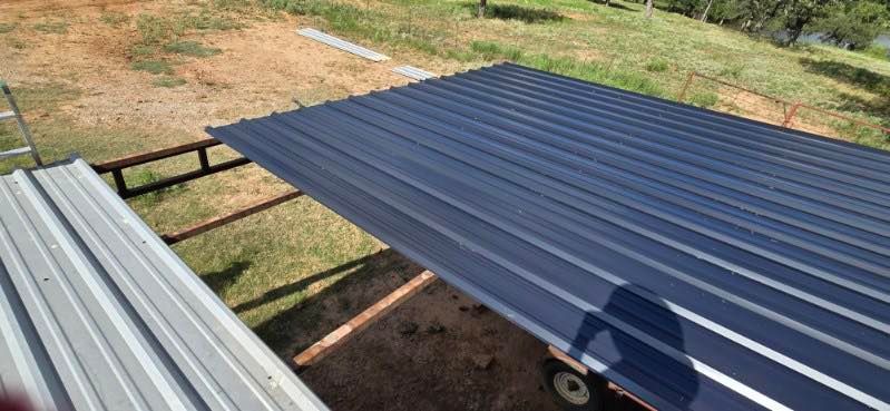 Blue corrugated metal roofing panels laid outdoors beside stacked silver panels