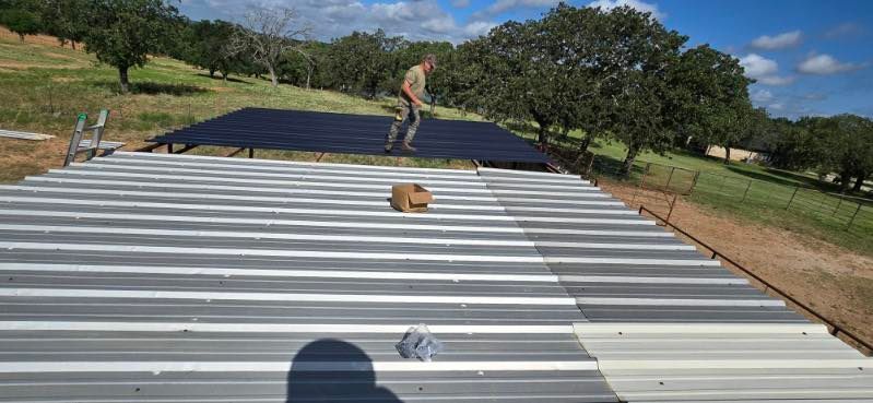 Person standing on a corrugated metal roof under construction in a grassy rural area